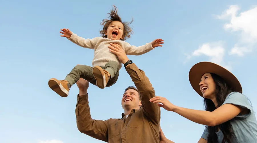 Pai levantando o filho no ar ao lado da mãe, todos sorrindo
